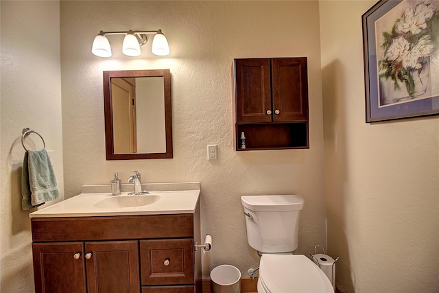half bathroom featuring toilet, vanity, and a textured wall