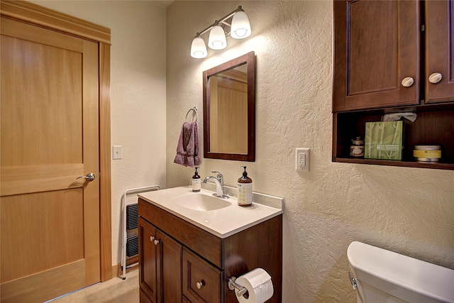 bathroom featuring vanity, toilet, a textured wall, and heating unit