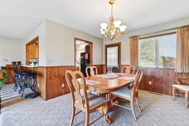 dining area featuring an inviting chandelier, light carpet, a textured ceiling, wainscoting, and wooden walls