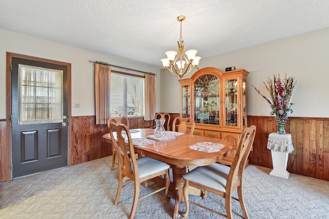 carpeted dining space with wooden walls, wainscoting, a chandelier, and a textured ceiling