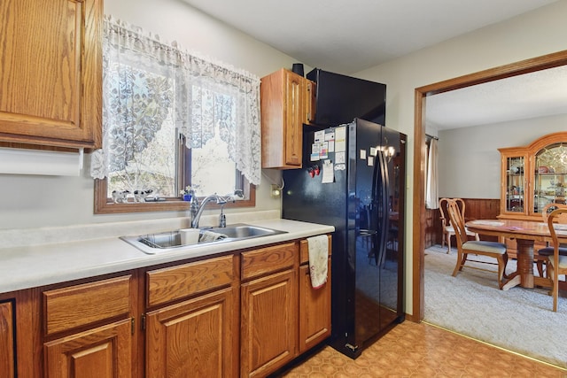 kitchen with a sink, brown cabinetry, black fridge with ice dispenser, light colored carpet, and light countertops