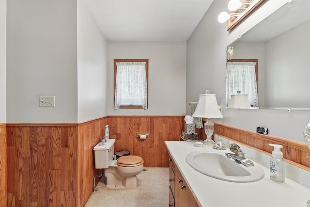 bathroom featuring toilet, wooden walls, vanity, and a wainscoted wall