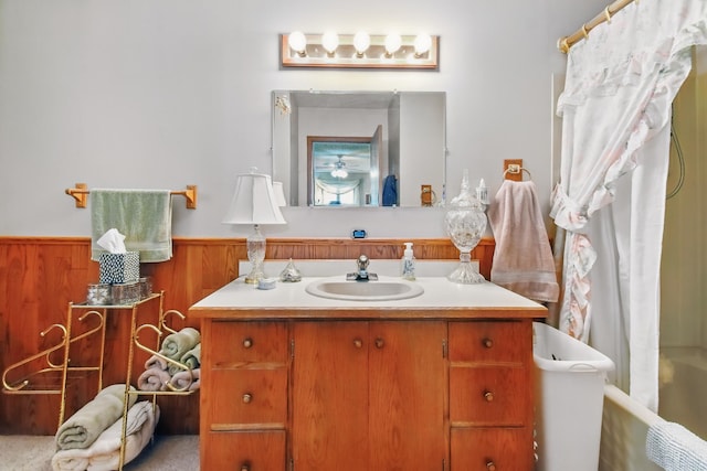 bathroom featuring curtained shower, wood walls, wainscoting, a tub, and vanity