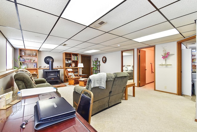 living area with a wood stove, visible vents, carpet floors, a paneled ceiling, and baseboards