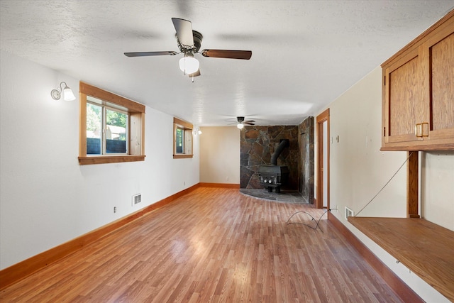 1108 9th St E, Polson, MT 59860 - unfurnished living room featuring a wood stove, light wood-type flooring, a ceiling fan, baseboards, and a textured ceiling