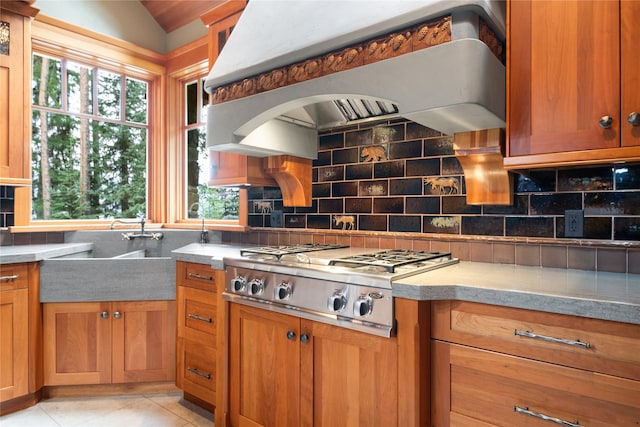 144 S Shore Pl, Seeley Lake, MT 59868 - kitchen featuring custom range hood, stainless steel gas stovetop, brown cabinetry, backsplash, and light tile patterned flooring