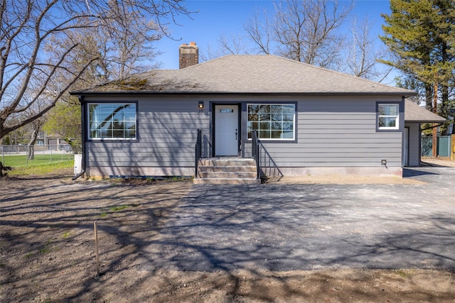 view of front of house with fence, roof with shingles, and a chimney