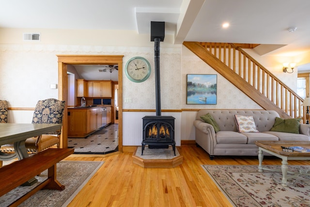 living area with ceiling fan, visible vents, light wood-style floors, stairway, and a wood stove