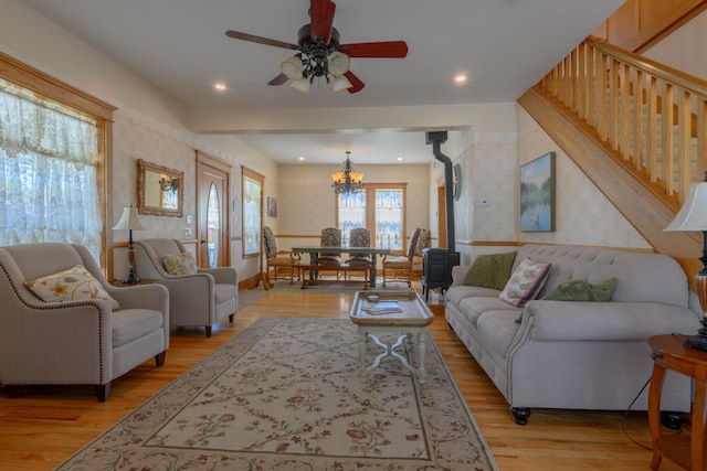 living area featuring a wood stove, light wood-style flooring, ceiling fan with notable chandelier, and recessed lighting