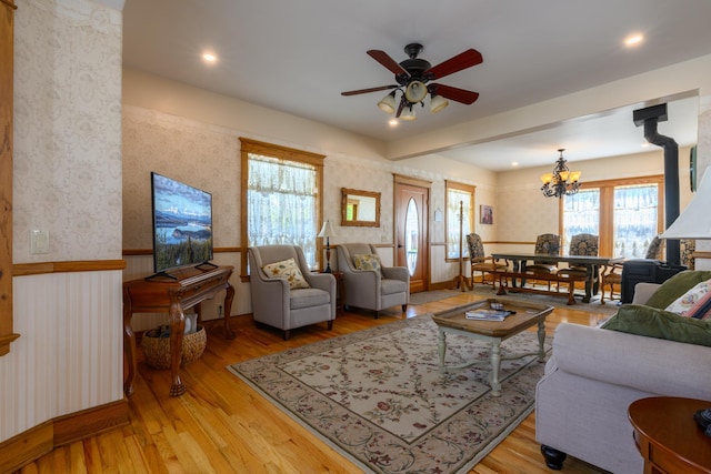 living area featuring light wood finished floors, wallpapered walls, and ceiling fan with notable chandelier