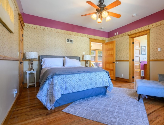 bedroom with wallpapered walls, visible vents, wood finished floors, and baseboards