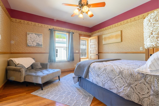 bedroom with wallpapered walls, wood finished floors, and ceiling fan