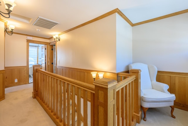 hallway with ornamental molding, an upstairs landing, visible vents, wooden walls, and wainscoting