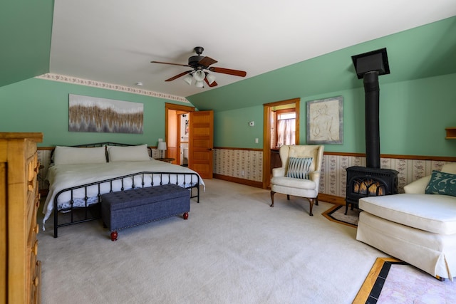 bedroom with a wood stove, carpet, vaulted ceiling, ceiling fan, and wainscoting