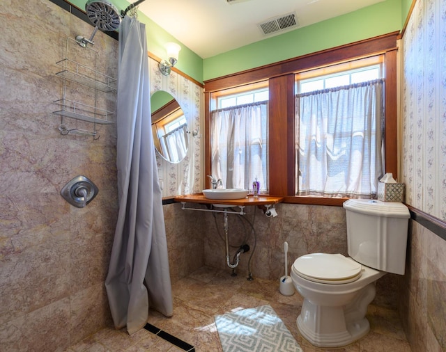 bathroom with a sink, toilet, tiled shower, and visible vents