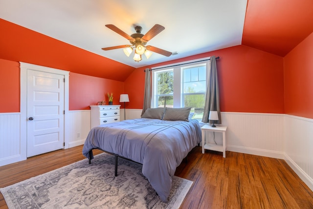 bedroom with wainscoting, vaulted ceiling, a ceiling fan, and wood finished floors
