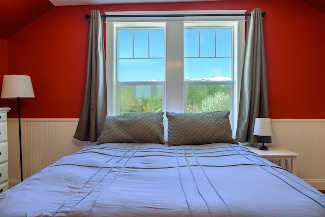 bedroom with wainscoting, vaulted ceiling, and multiple windows