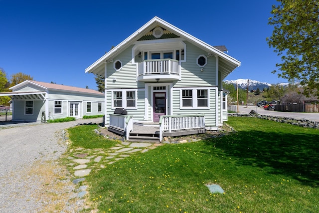 view of front facade with a front lawn, a deck with mountain view, gravel driveway, and a balcony
