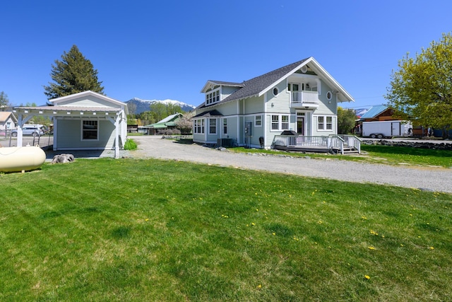 rear view of house with a mountain view, central AC, a yard, a balcony, and gravel driveway