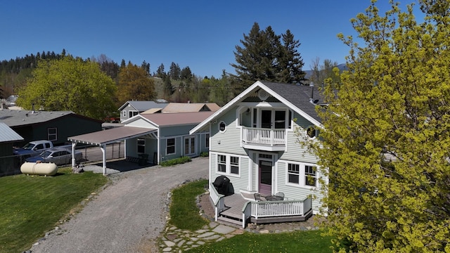exterior space featuring a balcony, driveway, a wooden deck, and a carport