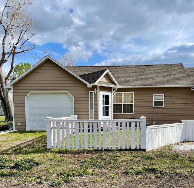 view of front of house with an attached garage, a shingled roof, fence, and a front lawn