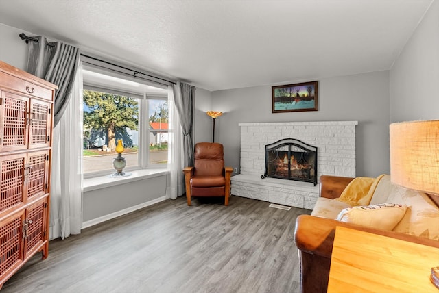 living room with a warm lit fireplace, visible vents, and wood finished floors