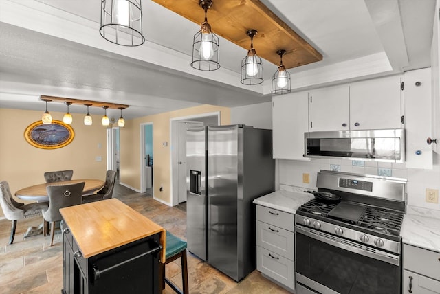 kitchen with pendant lighting, a kitchen island, a raised ceiling, tasteful backsplash, and appliances with stainless steel finishes