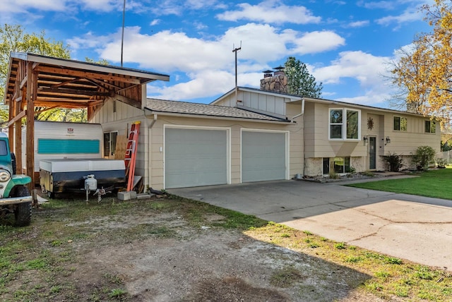 raised ranch with an attached garage, a chimney, board and batten siding, roof with shingles, and driveway