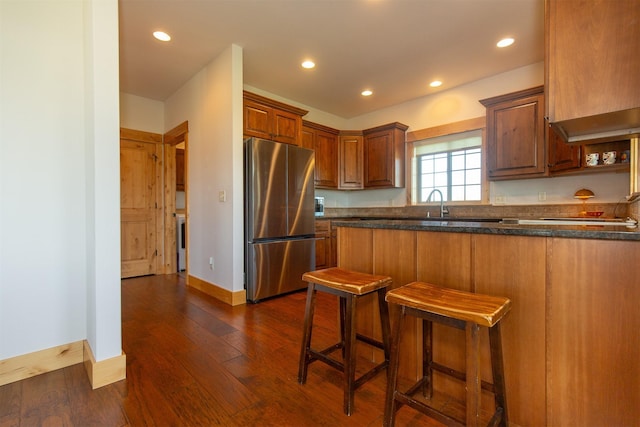 kitchen featuring freestanding refrigerator, recessed lighting, baseboards, a breakfast bar, and dark wood finished floors