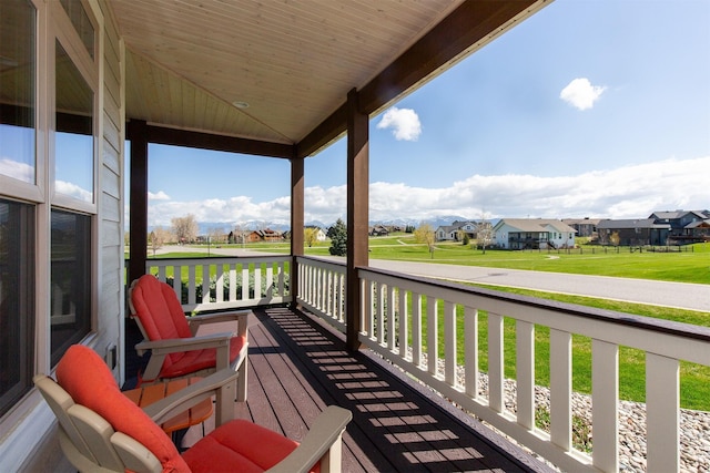 wooden deck featuring covered porch, a lawn, and a residential view