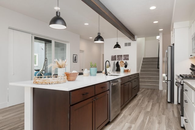 kitchen with light wood finished floors, light countertops, appliances with stainless steel finishes, and beam ceiling
