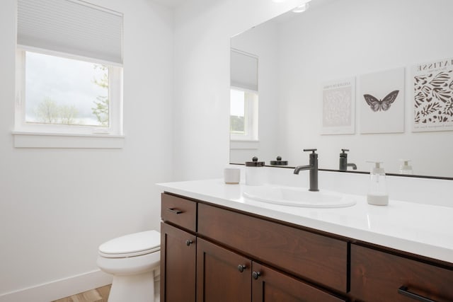 half bath with toilet, baseboards, vanity, and wood finished floors