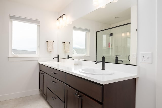full bath featuring a sink, double vanity, a stall shower, and baseboards