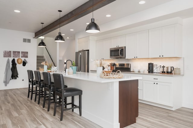 kitchen with light wood-style floors, beamed ceiling, a large island with sink, and appliances with stainless steel finishes
