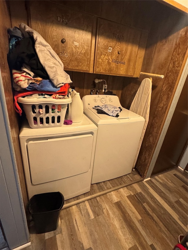 washroom featuring washing machine and dryer, cabinet space, and wood finished floors