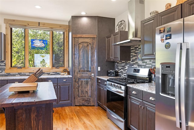 34426 Ridge Rd, Polson, MT 59860 - kitchen featuring appliances with stainless steel finishes, wall chimney exhaust hood, light wood finished floors, backsplash, and dark brown cabinetry