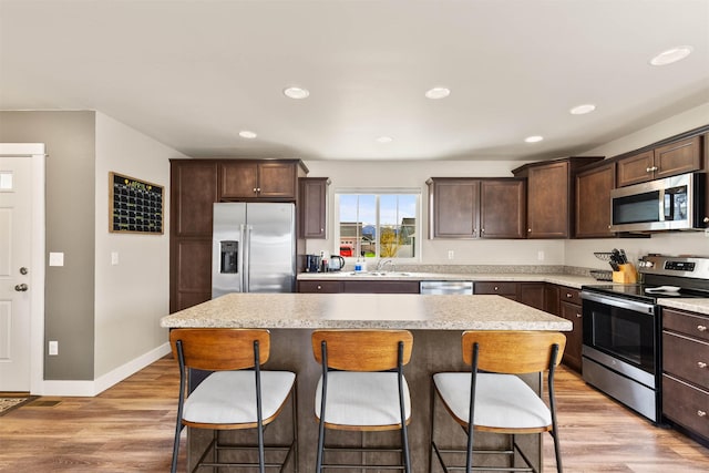 kitchen with a center island, dark brown cabinets, a kitchen bar, a sink, and stainless steel appliances