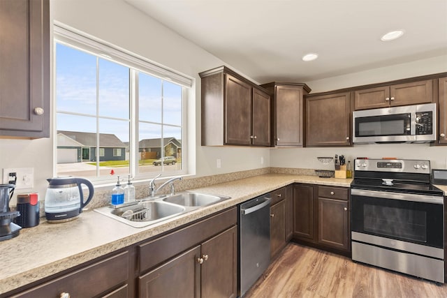 kitchen with stainless steel appliances, a sink, dark brown cabinetry, light countertops, and light wood-type flooring
