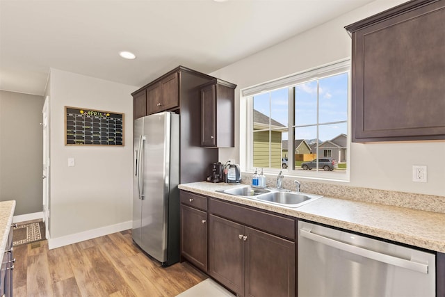 kitchen with stainless steel appliances, dark brown cabinets, light wood finished floors, a sink, and light countertops