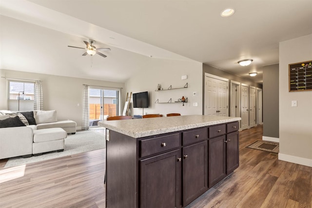 kitchen with light wood finished floors, a ceiling fan, baseboards, light countertops, and vaulted ceiling