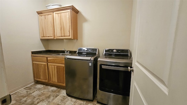 clothes washing area with stone finish floor, baseboards, a sink, washer and clothes dryer, and cabinet space