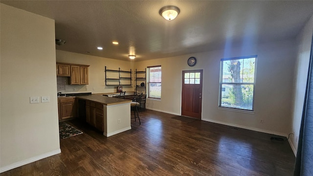 kitchen with a peninsula, a kitchen bar, dark wood-style floors, and baseboards