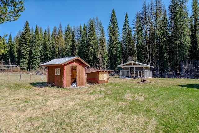 view of yard featuring a shed, a wooded view, an outdoor structure, and fence