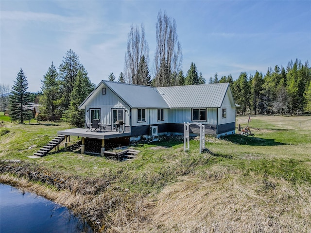 back of house featuring a lawn, metal roof, a deck with water view, and board and batten siding