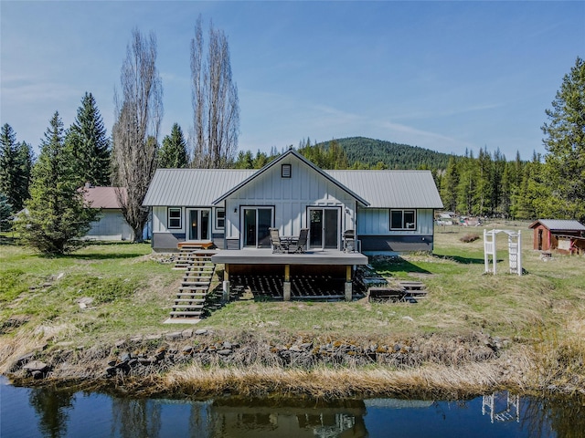rear view of property featuring a yard, board and batten siding, metal roof, a deck with water view, and stairs