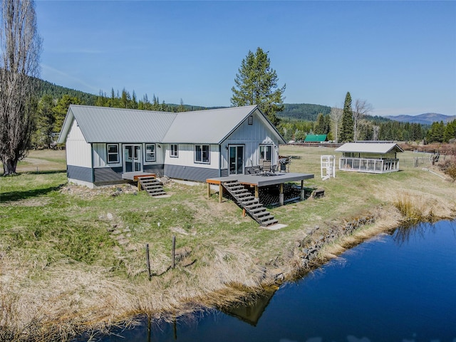 rear view of house featuring a deck with water view, stairs, metal roof, and a yard