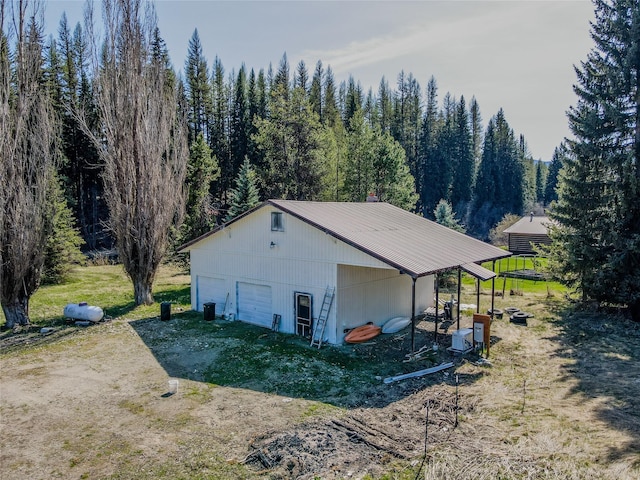 view of property exterior featuring a forest view, an outdoor structure, metal roof, and a garage