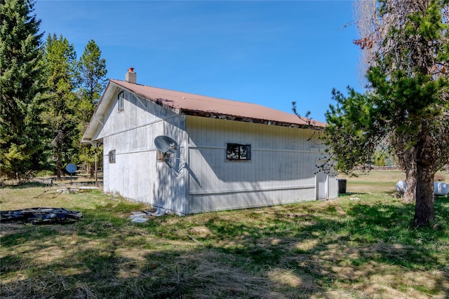 view of property exterior featuring a yard, a chimney, metal roof, and an outbuilding