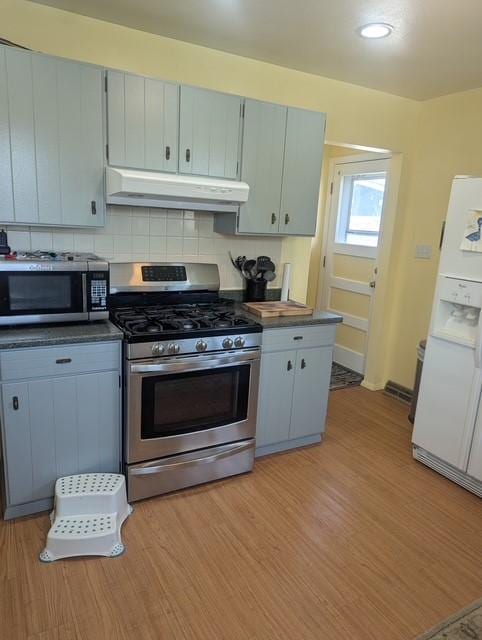 412 Raymond St, Helena, MT 59601 - kitchen with stainless steel appliances, under cabinet range hood, dark countertops, tasteful backsplash, and light wood-style flooring