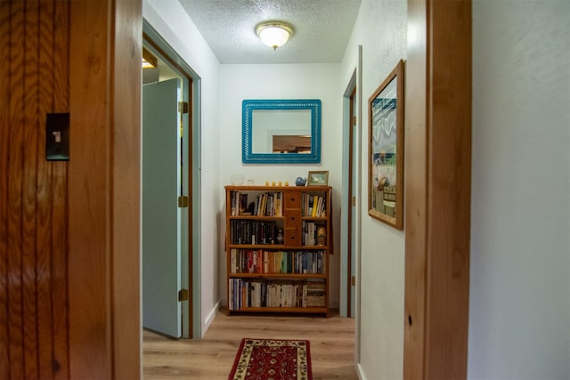 hall featuring a textured ceiling, wood finished floors, and baseboards